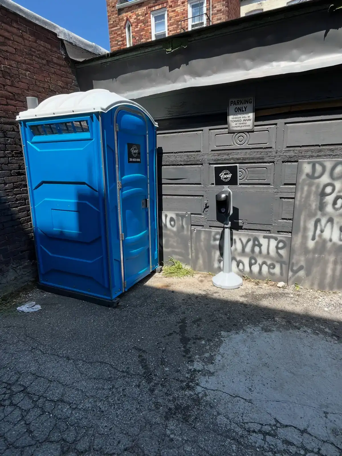Blue porta potty placed beside a brick building in a narrow alley