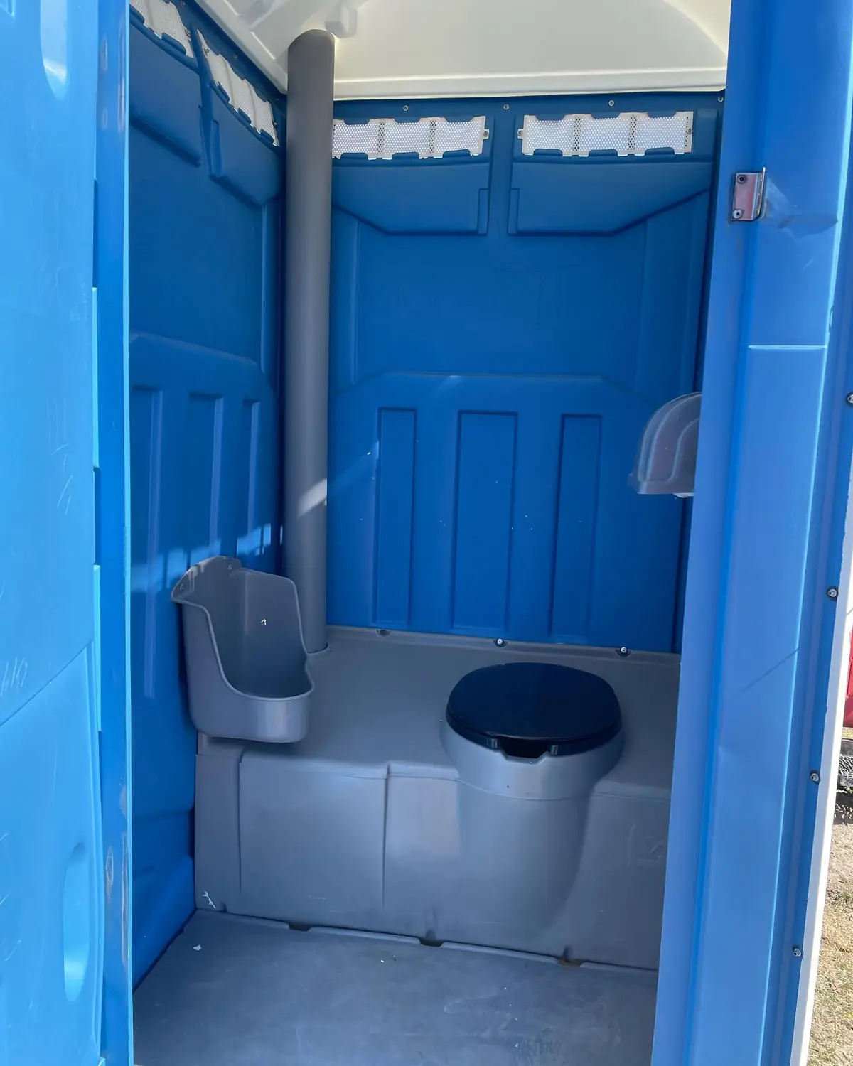 Inside a clean standard porta potty with seat, urinal and paper holder