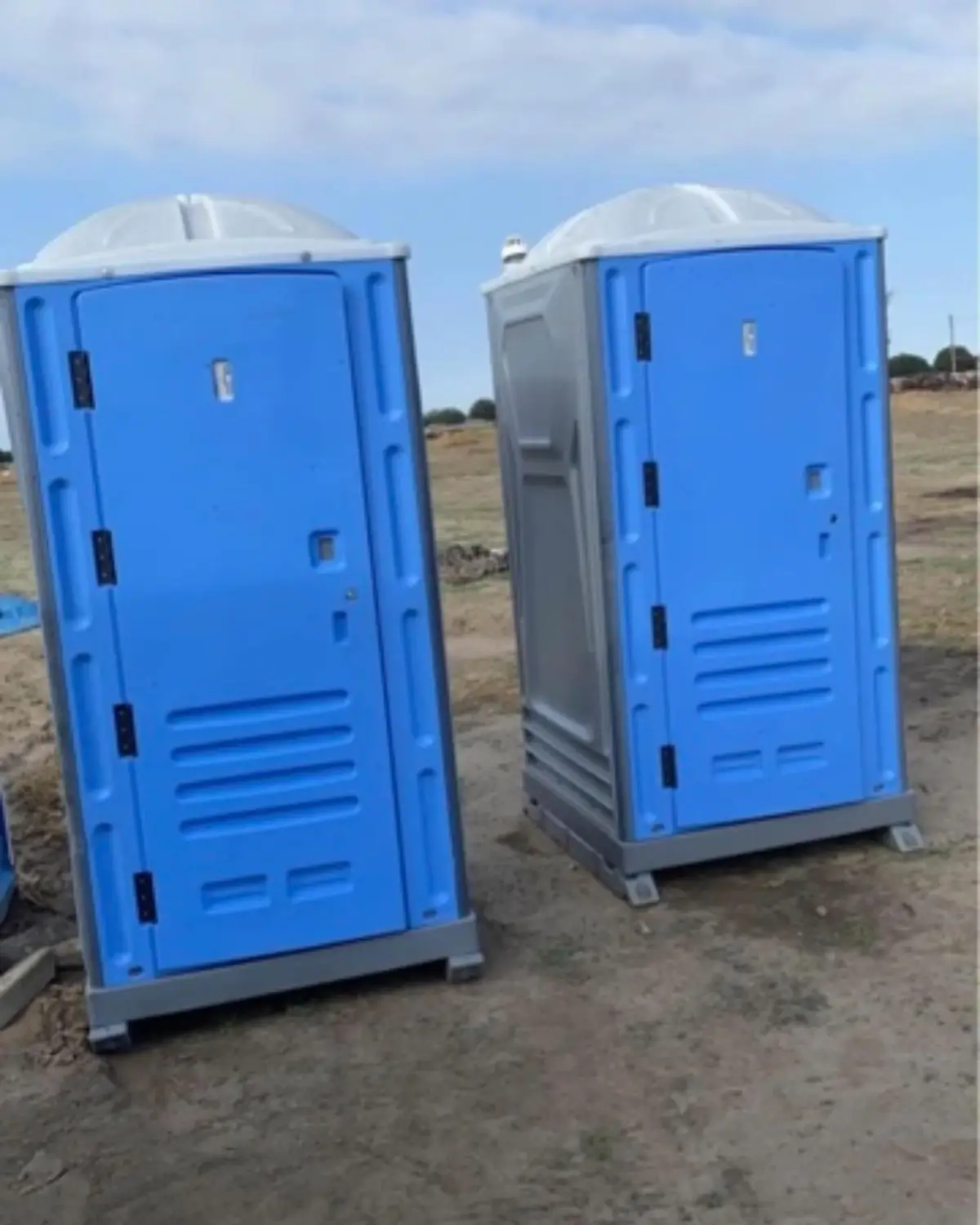 Two blue standard porta potties on level ground